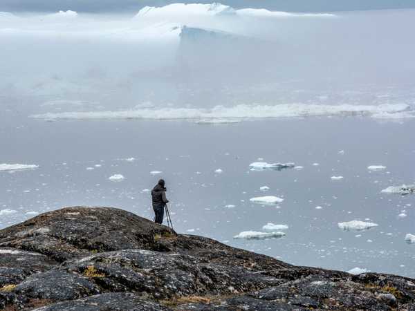 Un fotografo prepara lo scatto del Kangja Icefjord nella nebbia del mattino